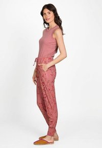 Woman standing sideways wearing a sleeveless pink striped top, pink floral pants with drawstring waist, and brown slip-on shoes.