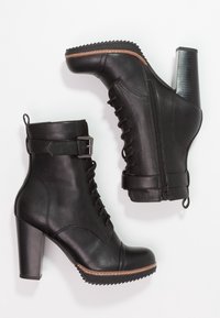 Botas negras hasta el tobillo con un acabado de cuero texturizado, cordones en la parte delantera, cremalleras laterales, detalle de hebilla y un tacón alto y grueso con una suela estriada.