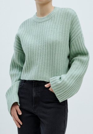 Minzgrüner, gerippter Pullover mit Rundhalsausschnitt und glockig geformten Ärmeln, kombiniert mit hochtaillierten, schwarzen Jeans. Weiche Textur.