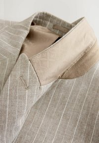 Blazer a righe color sabbia con fodera interna beige liscia caratterizzata da un delicato motivo floreale. Dettagli notevoli su revers e tasche in texture contrastanti.