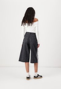 Juoda leopardo rašto kelnės-šortai su laisvu siluetu, aukštu liemeniu ir galinėmis kišenėmis. Derinamos su baltu off-shoulder topu ir juodais sportiniais batais.