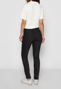 Witte kortekorte mouwen overhemd met een kraag, gecombineerd met zwarte slim-fit broek. De outfit is compleet met witte sneakers.