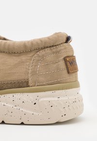 Hellbraune Leinenschuhe mit gepolstertem Kragen, beige gesprenkelter Sohle, einem tanfarbenen Lederlogo-Aufnäher und kontrastierenden Nähten.