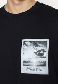 Černé tričko s černobílou grafikou městské siluety při západu slunce a textem "Miami Vibes" pod obrázkem.