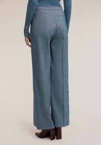 Wijde broek in een gestructureerde blauwe stof met een gladde afwerking. Heeft een hoge taille en subtiele plooien. Gepaard met bordeauxkleurige hakken.