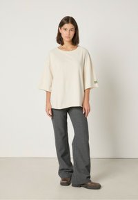 Jasnokremowy, oversize t-shirt z krótkimi rękawami i teksturowanym wykończeniem. Szare rozszerzane spodnie z delikatnym wzorem oraz ciemnobrązowe obuwie.