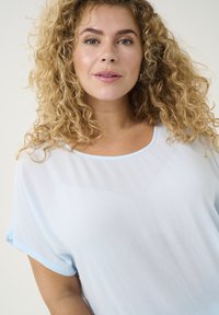 Blusa di un blu chiaro, comoda e ampia, con tessuto testurizzato, scollatura tonda e maniche corte con un orlo di un blu chiaro a contrasto.