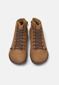 Zapatos de caña alta beige con cordones marrones y cremalleras laterales, exhibidos desde arriba sobre un fondo blanco.