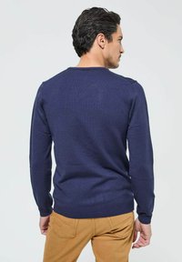 Pull en tricot bleu marine à manches longues avec un col ras du cou. Le matériau semble doux avec une texture lisse, une coupe ajustée et des poignets côtelés.