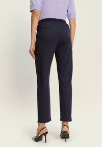 Middengraanblauwe tapered broek gemaakt van zachte stof, met een elastische tailleband en twee achterzakken, gestyled met hoge hakken.