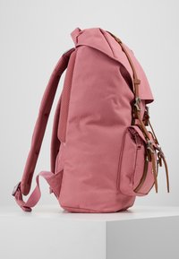 Sac à dos en tissu rose avec une forme structurée, accents en cuir beige, bretelles ajustables et poche latérale. Comprend un mesh respirant sur les bretelles.