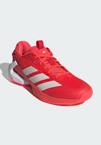 Červená sportovní bota s prodyšným síťovaným svrškem, logo s třemi bílými pruhy, ploché tkaničky a silná podešev s výrazným designem paty.