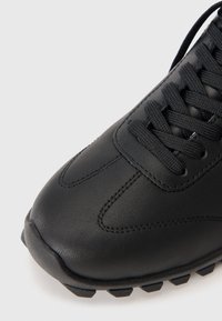 Black athletic shoe with a smooth leather upper, round toe, textured laces, and a rubber outsole featuring a traction pattern.