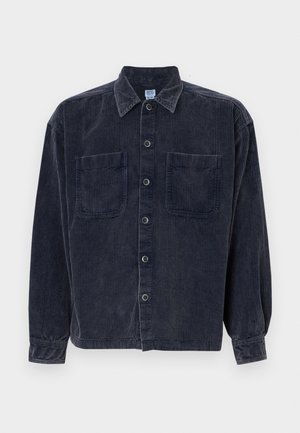 Camisa de pana azul marino con mangas largas, dos bolsillos frontales y cierre de botones. Presenta un collar clásico y una tela texturizada.