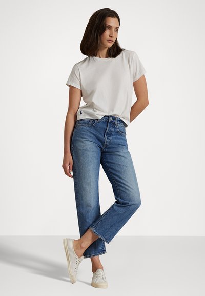 Vit bomull t-shirt i avslappnad passform, kombinerad med ljusblå raka jeans med fransad nederkant. Krämfärgade sneakers fulländar outfiten.