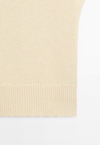 Gros plan sur un tissu tricoté de couleur crème avec un motif texturé et un ourlet côtelé sur un fond uni.