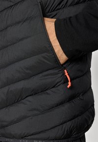 Μαύρο γιλέκο με πούπουλα και διαγώνιο ραφτό σχέδιο. Διαθέτει πλαϊκή τσέπη με πορ�τοκαλί κορδόνι που αναδεικνύει την υφή και τη λάμψη του υφάσματος.