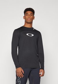 Langermet svart treningsskjorte med teksturert stoff, rund hals og en fremtredende hvit logo på brystet, designet for sportsytelse.
