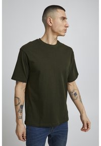 Mørkegrøn t-shirt med rund halsudskæring og korte ærmer. Stoffet ser blødt og glat ud, bæres med blå denim jeans.