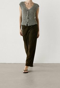 Cardigan in maglia a maniche corte grigio e bianco, con scollo a V e bottoni frontali, abbinato a pantaloni larghi marrone scuro e sandali neri.