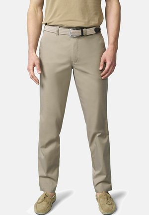 Mann trägt beige Freizeithose, passenden gewebten Gürtel und Wildleder-Mokassin-Schuhe und steht mit entspannten Händen an den Seiten.