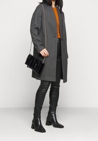 Šedý kabát rybí kost, volný střih, zapínání na jeden knoflík. Černá prošívaná kabelka s řetízkovým popruhem. Černé kožené přiléhavé kalhoty a kotníkové boty.