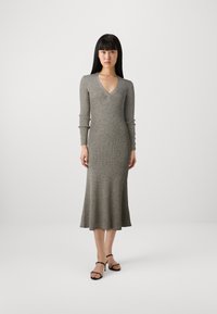 Robe tricotée gris à côtes avec décolleté en V, manches longues et ourlet festonné ; accompagnée de sandales noires à lanières avec accents métalliques.