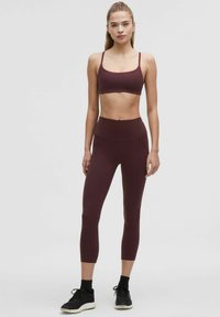 Sostén deportivo granate y leggings de cintura alta a juego, hechos de una tela suave, con un diseño ajustado, combinados con zapatillas deportivas negras.