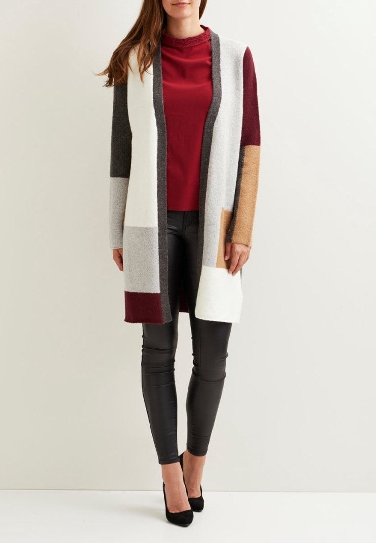 Cardigan en maille présentant des panneaux multicolores en gris, blanc, bordeaux et beige. Porté sur un haut bordeaux, associé à des leggings noirs et des talons.