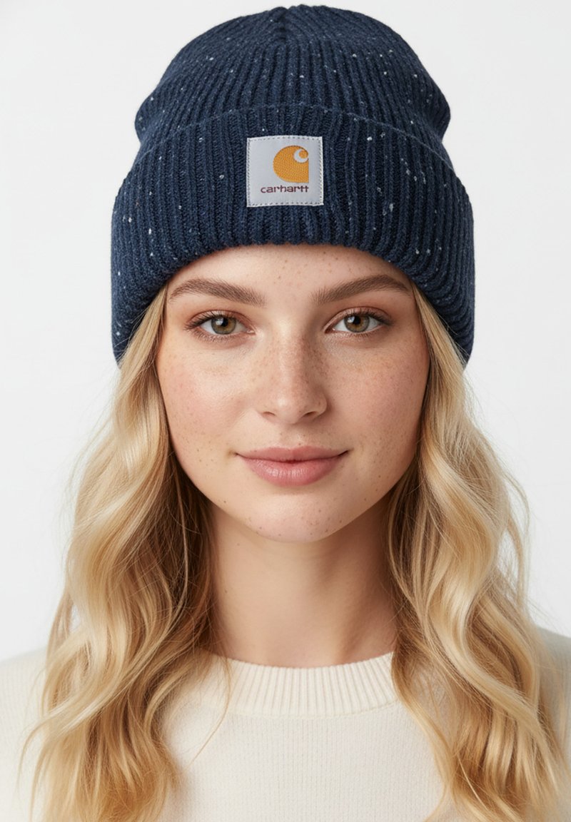 Gorro de punto acanalado color azul marino con motas de color, que presenta un parche cuadrado con un logo. Textura suave, ajuste casual para abrigar.