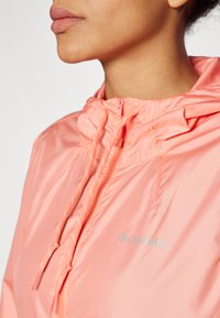 Lightweight, hooded jacket in bright coral with a shiny finish, featuring drawstrings, zip closure, and a small Columbia logo.