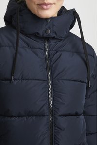 Giacca imbottita blu navy con colletto alto, zip nera e lacci. Presenta sezioni trapuntate e una superficie liscia nel tessuto.