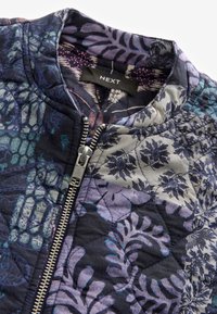 Chaqueta bomber acolchada en azul marino con patrones florales en púrpura y gris, que cuenta con una cremallera plateada y un cuello alzado.