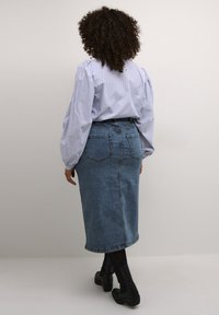 Denim midi-rok met een aansluitende taille, achterzakken en een rechte snit, gecombineerd met een blauw-wit gestreepte blouse en zwarte enkellaarsjes.