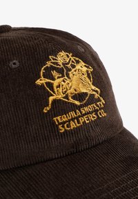 Gorra de pana marrón con un diseño bordado en dorado que incluye el texto "Tequila Shots" y "Scalpers Co." en la parte frontal.