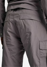 Šedé cargo kalhoty s hladkou matnou texturou, několika kapsami a zakřiveným švem po straně pro zvýšený styl.