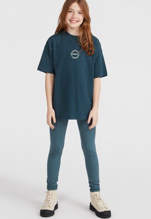 Teal oversize t-särk koos logoga, millele on paaritatud teal värvi retuusid. Mudel kannab beeže nööridega saapaid, millel on tekstureeritud tallad. Lihtne, mugav rõivastus.