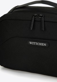 Zwarte toilettas gemaakt van gestructureerde stof. Bevat dubbele ritsen met "Wittchen" merk en heeft een plat ontwerp voor gemakkelijke opslag.