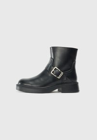 Botte de cheville en cuir noir avec un bout arrondi, une boucle en métal argenté et un talon empilé. Texture lisse, design minimaliste.
