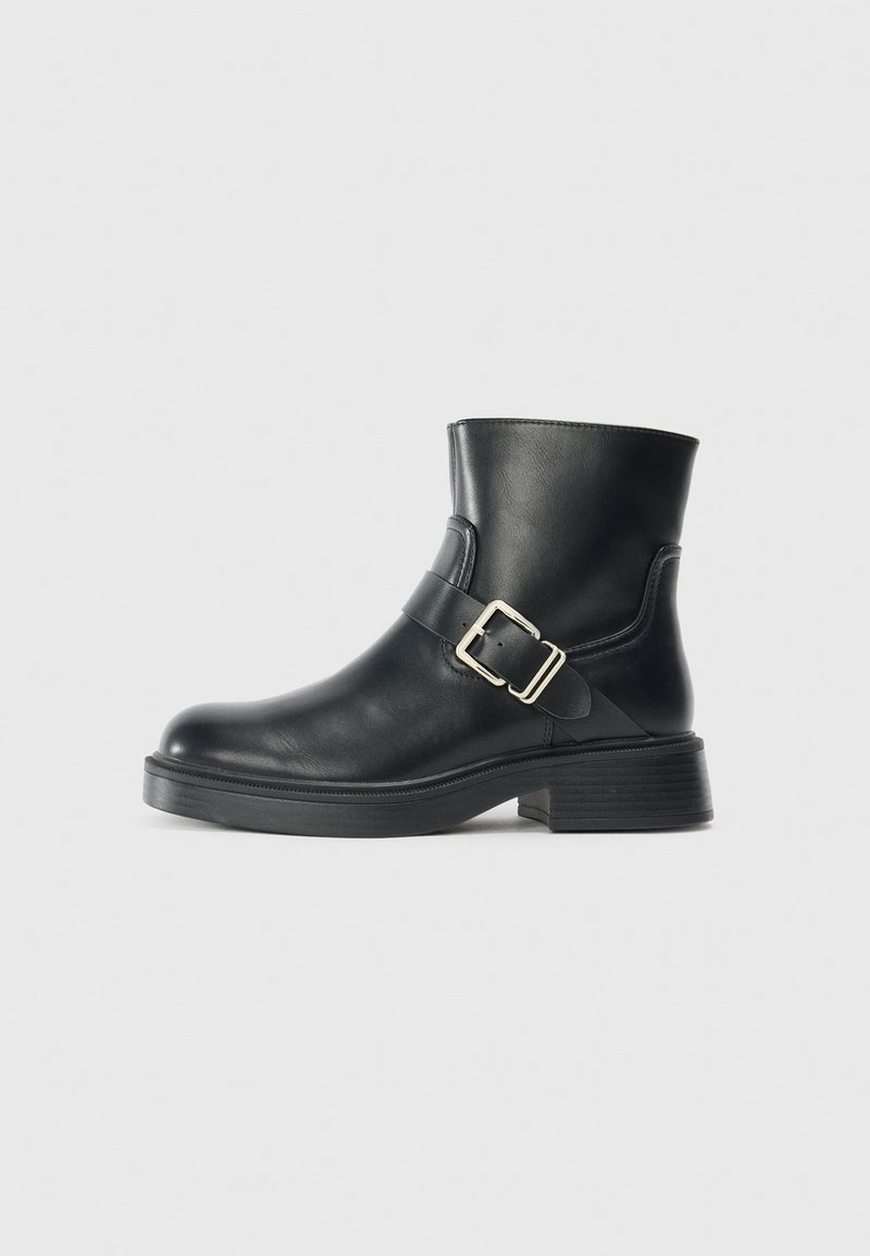 Botte de cheville en cuir noir avec un bout arrondi, une boucle en métal argenté et un talon empilé. Texture lisse, design minimaliste.