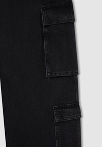 Czarne spodnie cargo wykonane z denimu o gładkiej fakturze. Posiadają dwie boczne kieszenie z klapami oraz wykończenia haftowane.