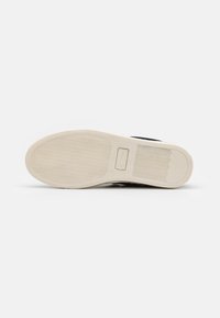 Zwarte sneaker met een gestructureerde rubberen zool, voorzien van een glad bovenwerk, versterkte neus en subtiele branding aan de zijkant.
