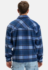 Blue plaid fleece shirt jacket with a button-up front, featuring varying shades of blue and black checks, and a slightly textured finish.