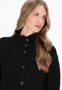 Czarny sweter dzianinowy z wysokim kołnierzem, dekoracyjnym wzorem w zygzaki i pięcioma dużymi okrągłymi guzikami z przodu.