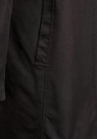 Czarna, matowa tkanina o gładkiej fakturze z boczną kieszenią i detalem złożonego rękawa. Ubranie ma minimalistyczny design i prosty krój.