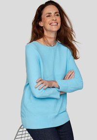 Helle blaue Strickjacke mit Rundhalsausschnitt, langen Ärmeln und gerippten Bündchen; kombiniert mit dunkelblauen Jeans. Glatte Textur, lässiges Design.