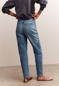 Világoskék farmernadrág laza szabással és öt zsebbel, hozzá lágy rózsaszín balettcipő pánttal a lábfején.