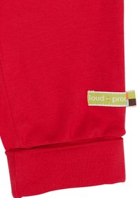 Rote Baumwollsweatpants mit gerippten Bündchen und einem kleinen, mehrfarbigen Etikett mit der Aufschrift "loud + proud", das an der Seitennaht befestigt ist.