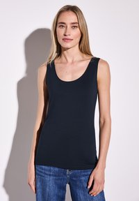 Marineblaues ärmelloses Oberteil mit Rundhalsausschnitt, aus weichem, dehnbarem Stoff. Kombiniert mit hellblauen Jeans.