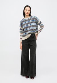 Gebreide trui met meerkleurige geometrische patronen; losse pasvorm. Gecombineerd met zwart wijde pijpen jeans met hoge taille en donkere schoenen.